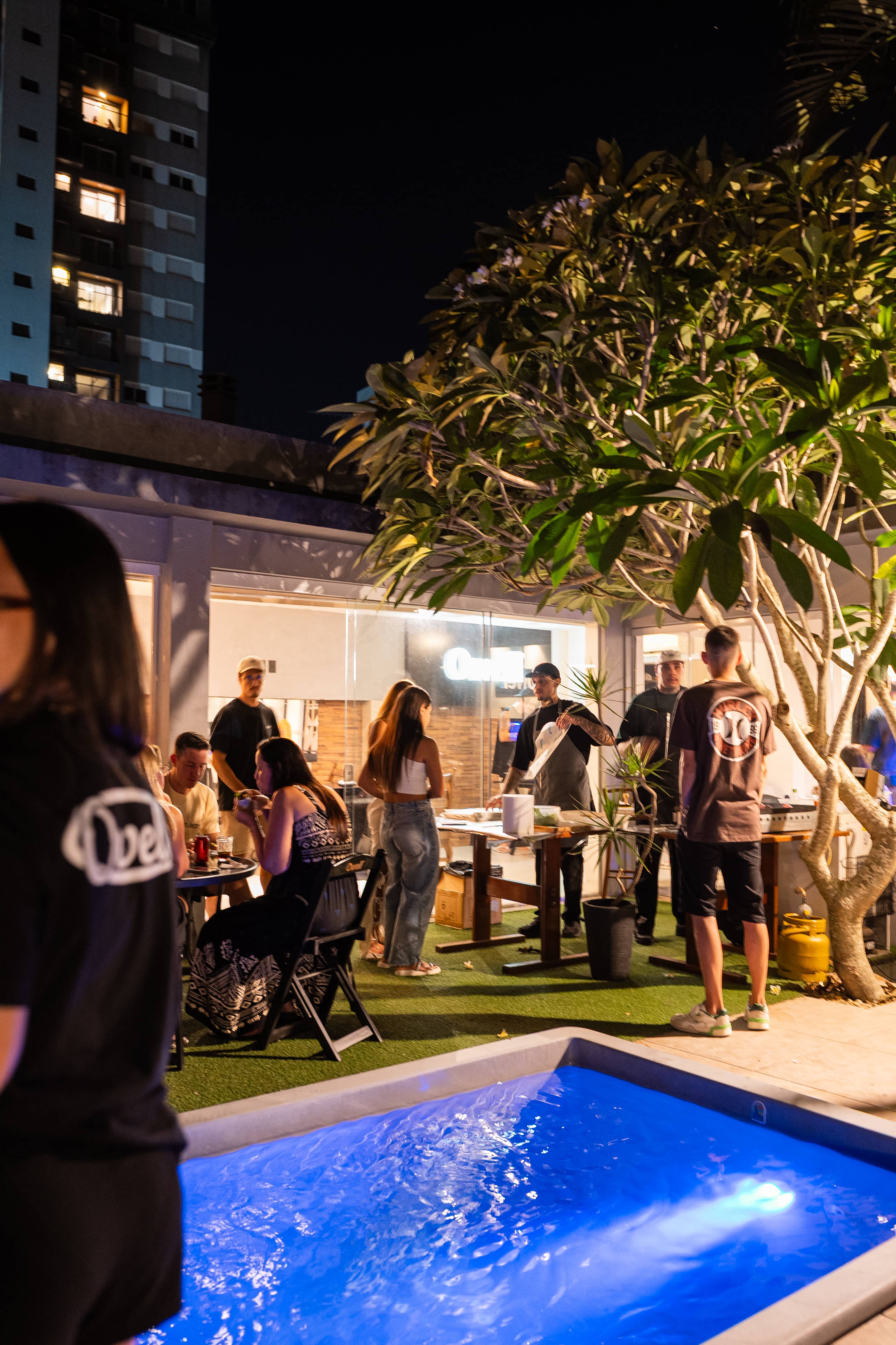 Noite na Owell's House, piscina iluminada de azul e gente reunida